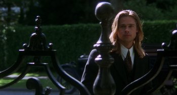 Movie still from “Legends of the Fall” (1994), directed by Edward Zwick – A man wearing a suit and tie standing next to a fence; Medium shot, Low angle