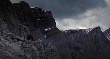 Movie still from “Legends of the Fall” (1994), directed by Edward Zwick – A person sitting on a rock on top of a mountain; Extreme Wide shot, Low angle
