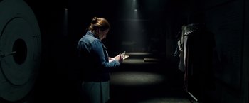Movie still from “Lights Out” (2016), directed by David F. Sandberg – A woman standing in the dark looking at her cell phone; Medium shot, Over the shoulder angle