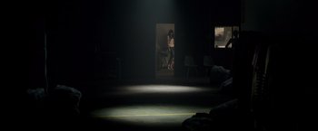 Movie still from “Lights Out” (2016), directed by David F. Sandberg – A person standing in a dark room with chairs around them; Wide shot, Low angle