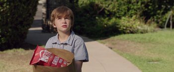 Movie still from “Lights Out” (2016), directed by David F. Sandberg – A young boy holding a bag of potato chips on the sidewalk; Medium shot, Over the shoulder angle