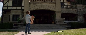 Movie still from “Lights Out” (2016), directed by David F. Sandberg – A young boy holding a paper bag in front of a building; Wide shot, Low angle