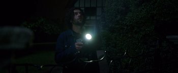 Movie still from “Lights Out” (2016), directed by David F. Sandberg – A man holding a flashlight while standing next to a bush; Medium shot, Low angle