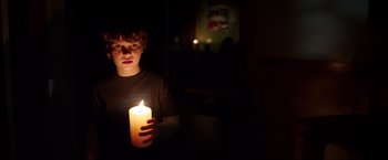 Movie still from “Lights Out” (2016), directed by David F. Sandberg – A boy holding a lit candle in a dark room; Medium shot, Over the shoulder angle