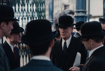 Movie still from “Living” (2022), directed by Oliver Hermanus – A group of men in suits and hats standing next to each other; Medium shot, Over the shoulder angle