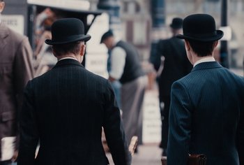 Movie still from “Living” (2022), directed by Oliver Hermanus – A group of men in suits and hats walking down a street; Medium shot, Over the shoulder angle