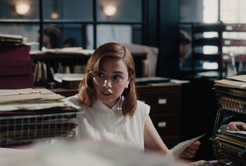 Movie still from “Living” (2022), directed by Oliver Hermanus – A woman sitting at a desk in a room; Medium shot, Over the shoulder angle