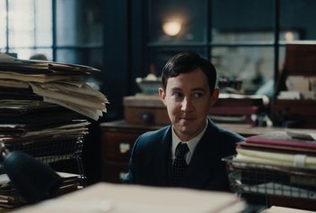 Movie still from “Living” (2022), directed by Oliver Hermanus – A man sitting at a desk in front of a stack of papers; Medium shot, High angle