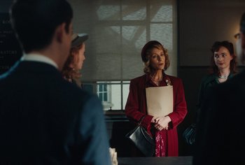 Movie still from “Living” (2022), directed by Oliver Hermanus – An older woman wearing a red coat and a hat; Medium shot, Over the shoulder angle