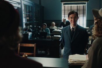 Movie still from “Living” (2022), directed by Oliver Hermanus – A man in a suit standing in front of a table; Medium shot, Over the shoulder angle