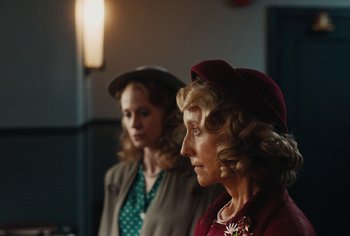 Movie still from “Living” (2022), directed by Oliver Hermanus – Two women are standing next to each other in a room; Close Up shot, Over the shoulder angle
