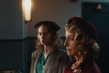 Movie still from “Living” (2022), directed by Oliver Hermanus – Two women are standing next to each other in a room; Close Up shot, Over the shoulder angle