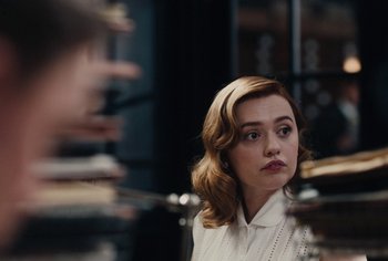 Movie still from “Living” (2022), directed by Oliver Hermanus – A young woman in a white shirt is looking at the camera; Close Up shot, Over the shoulder angle