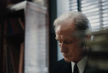 Movie still from “Living” (2022), directed by Oliver Hermanus – An older man wearing a suit and tie; Close Up shot, Over the shoulder angle
