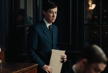 Movie still from “Living” (2022), directed by Oliver Hermanus – A man in a suit holding a piece of paper; Medium shot, Low angle