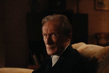 Movie still from “Living” (2022), directed by Oliver Hermanus – An older man sitting on a couch in a room; Close Up shot, High angle