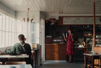 Movie still from “Living” (2022), directed by Oliver Hermanus – A woman in a red dress stands in front of a man in a red dress; Wide shot, Over the shoulder angle