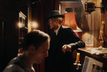 Movie still from “Living” (2022), directed by Oliver Hermanus – A man wearing a suit and a hat standing next to a man; Medium shot, Over the shoulder angle