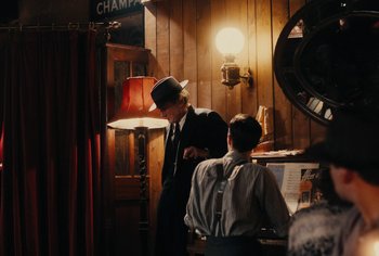 Movie still from “Living” (2022), directed by Oliver Hermanus – A man in a suit and hat standing next to a woman in a hat; Medium shot, Over the shoulder angle