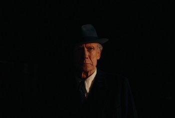 Movie still from “Living” (2022), directed by Oliver Hermanus – An old man wearing a suit and a hat in the dark; Close Up shot, Low angle