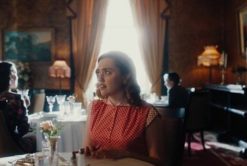 Movie still from “Living” (2022), directed by Oliver Hermanus – A woman sitting at a table in front of a window; Medium shot, Over the shoulder angle