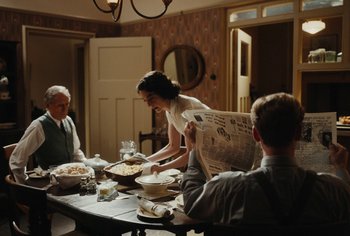 Movie still from “Living” (2022), directed by Oliver Hermanus – A group of people sitting around a table with food on top of it; Medium shot, High angle