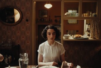 Movie still from “Living” (2022), directed by Oliver Hermanus – A woman sitting at a table with a plate in front of her; Medium shot, Over the shoulder angle
