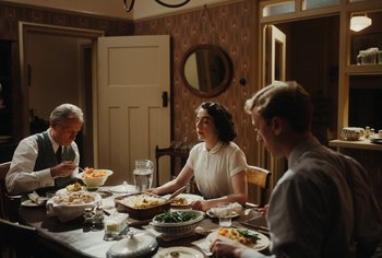 Movie still from “Living” (2022), directed by Oliver Hermanus – A group of people sitting around a table with food; Medium shot, High angle