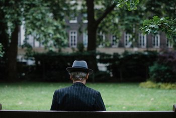 Movie still from “Living” (2022), directed by Oliver Hermanus – An older man sitting on a bench in a park; Medium shot, Over the shoulder angle