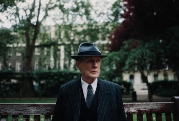 Movie still from “Living” (2022), directed by Oliver Hermanus – An older man wearing a suit and a hat; Close Up shot, Over the shoulder angle