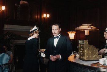 Movie still from “Living” (2022), directed by Oliver Hermanus – A man and a woman standing in front of a counter; Medium shot, Low angle