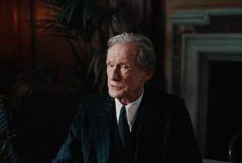 Movie still from “Living” (2022), directed by Oliver Hermanus – An older man wearing a suit and tie; Close Up shot, Over the shoulder angle