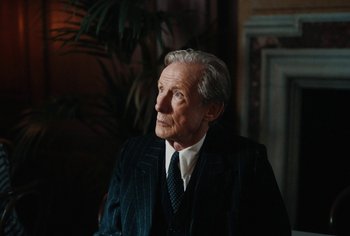 Movie still from “Living” (2022), directed by Oliver Hermanus – An older man wearing a suit and tie; Medium shot, Over the shoulder angle