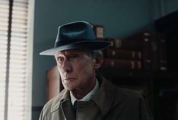 Movie still from “Living” (2022), directed by Oliver Hermanus – An older man wearing a hat and a coat; Close Up shot, Over the shoulder angle