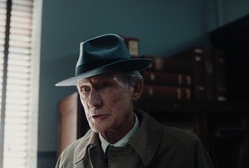 Movie still from “Living” (2022), directed by Oliver Hermanus – An older man wearing a hat and a jacket; Close Up shot, Over the shoulder angle