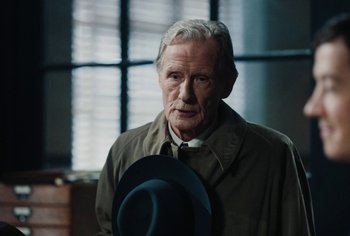 Movie still from “Living” (2022), directed by Oliver Hermanus – An older man wearing a hat in a room; Close Up shot, Over the shoulder angle