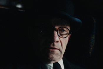Movie still from “Living” (2022), directed by Oliver Hermanus – A man in a suit and hat with glasses and a tie; Close Up shot, Over the shoulder angle