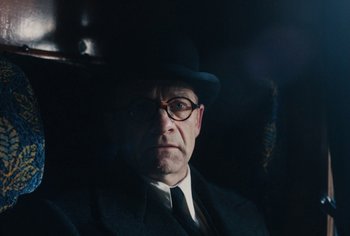 Movie still from “Living” (2022), directed by Oliver Hermanus – A man in a suit and hat is sitting in a car; Close Up shot, Over the shoulder angle