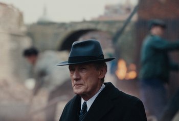 Movie still from “Living” (2022), directed by Oliver Hermanus – An older man wearing a hat and a suit; Close Up shot, Over the shoulder angle