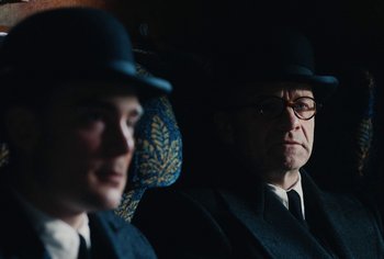 Movie still from “Living” (2022), directed by Oliver Hermanus – A man in a suit and a hat sitting next to another man in a suit; Close Up shot, Over the shoulder angle