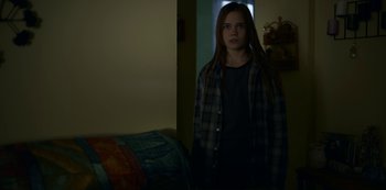 Movie still from “Lost Girls” (2020), directed by Liz Garbus – A young girl standing in a dark room; Medium shot, Over the shoulder angle
