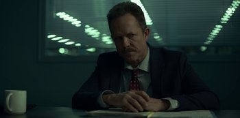 Movie still from “Lost Girls” (2020), directed by Liz Garbus – A man sitting at a table in a suit and tie; Close Up shot, Low angle