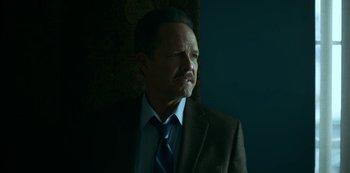 Movie still from “Lost Girls” (2020), directed by Liz Garbus – A man wearing a suit and tie in a dark room; Close Up shot, Low angle