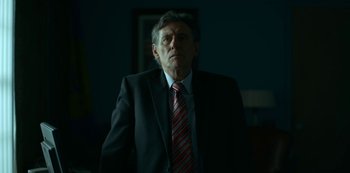 Movie still from “Lost Girls” (2020), directed by Liz Garbus – A man wearing a suit and tie standing in a room; Close Up shot, Low angle