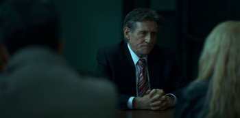 Movie still from “Lost Girls” (2020), directed by Liz Garbus – A man in a suit and tie sitting at a table; Close Up shot, Over the shoulder angle