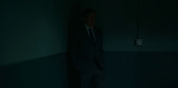 Movie still from “Lost Girls” (2020), directed by Liz Garbus – A man in a suit standing in a dark room; Medium shot, Low angle