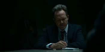 Movie still from “Lost Girls” (2020), directed by Liz Garbus – A man sitting at a table writing on a piece of paper; Close Up shot, Low angle