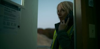 Movie still from “Lost Girls” (2020), directed by Liz Garbus – A woman in a yellow vest talking on a cell phone; Close Up shot, Low angle
