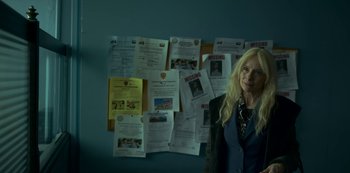 Movie still from “Lost Girls” (2020), directed by Liz Garbus – A woman standing in front of a wall of missing posters; Medium shot, High angle