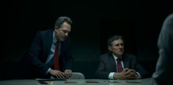 Movie still from “Lost Girls” (2020), directed by Liz Garbus – Two businessmen sitting at a table in front of each other; Medium shot, Over the shoulder angle